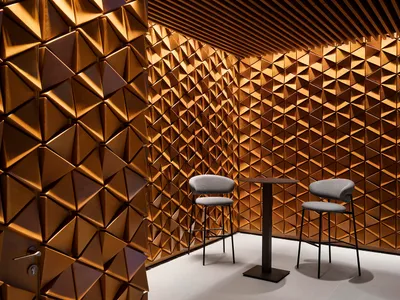 A cozy seating area with two chairs placed on a carpeted floor in front of a wall with a unique, possibly wood or textured surface design
