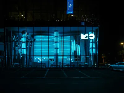 A modern restaurant interior with glass walls, blue lights, and minimalist design, featuring a dining area with chairs and tables