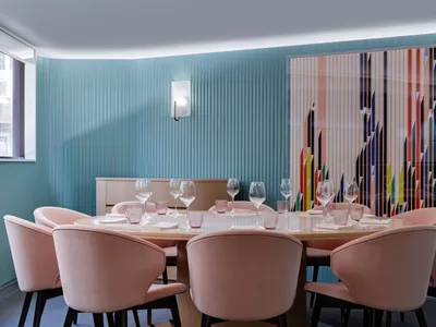 A dining area with a long pink table set for a meal, surrounded by chairs and wine glasses, creating a warm and inviting ambiance