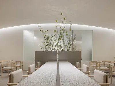A clean and inviting restaurant interior with a long dining table, chairs, and potted plants