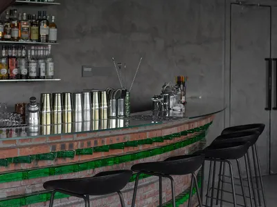 A modern bar with a green marble countertop, stools, and bottles displayed, set in a sophisticated restaurant atmosphere