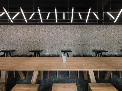 A modern restaurant interior with a large wooden dining table surrounded by multiple chairs, featuring a warm and inviting ambiance with natural materials and clean lines