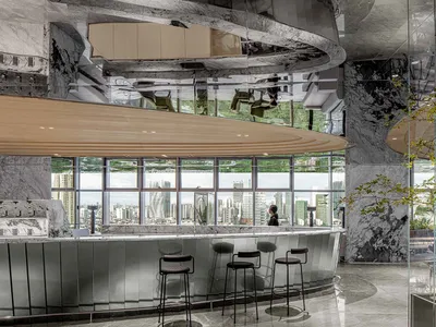 A modern bar area with a curved marble counter, stools, chairs, and tables, creating a sophisticated and inviting atmosphere