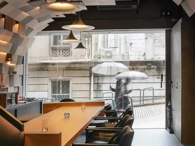 A modern restaurant interior with a large dining table, multiple chairs, and potted plants, creating a comfortable seating area