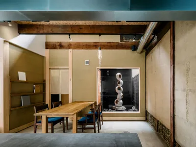 Warm and inviting dining area with a wooden table and chairs, connected to a kitchen space with a sink in the background, lit by natural light