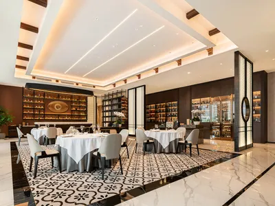 Modern restaurant interior with marble flooring, black and white decor, potted plants, and dim lighting