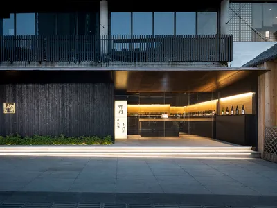 Contemporary Asian restaurant with a black facade, glass front door, and a spacious interior featuring a bar area with wine bottles and potted plants