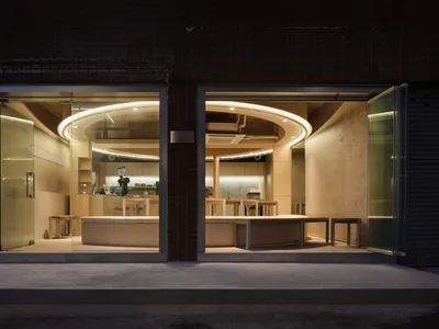 Open restaurant interior with wooden floors and walls, natural light from large windows, and dining tables with chairs and tableware