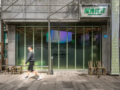 一間帶有大型玻璃窗的店面展示商品，門外有兩張椅子，一人走過