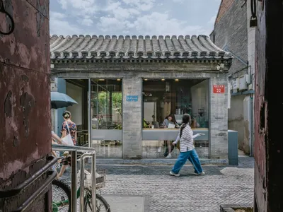 A lively Asian restaurant with a brick facade, featuring a large archway entrance, dining tables, chairs, and potted plants, with people enjoying their meals