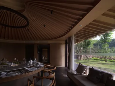 Cozy restaurant interior with a dining area and living room featuring a round table, chairs, couch, and bench, with wine glasses and a warm atmosphere