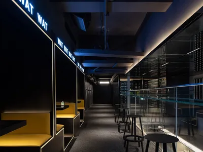 A modern restaurant or bar area with a long hallway featuring benches and chairs, overhead lighting, and a welcoming atmosphere