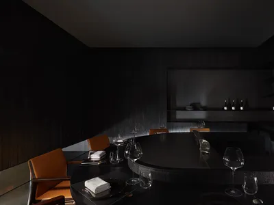 A dark and moody restaurant dining area with a table and chairs, wine glasses, and scattered bottles