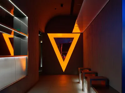 Dimly lit room with a large triangle shape, chairs placed around the space, and a contemporary feel