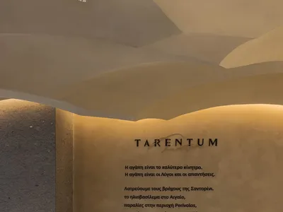 A modern restaurant dining area with tables, chairs, and vases, featuring Greek text on the walls and a stylish atmosphere