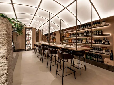 A spacious restaurant dining area with tables, chairs, and wine bottles on display, set in a warm and inviting atmosphere