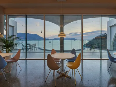 Dining area with a large window offering an ocean view, featuring a white table and various chairs with a yellow seat in a modern and inviting atmosphere