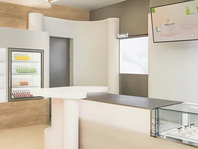 A casual cafe interior with a counter featuring a refrigerator and bottles, cups, and a welcoming atmosphere