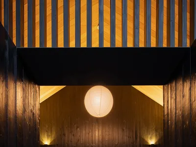 A warm and cozy living dining space with wooden walls, a central bench, and a round light fixture