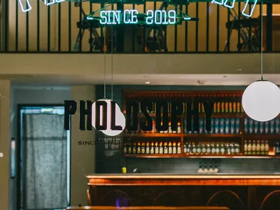 A restaurant interior with a bar area and dining tables, featuring a warm and inviting atmosphere with bottles on the counter and chairs around the tables