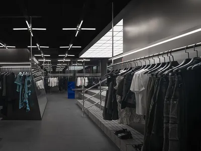 A dark and empty retail space with white walls and a black ceiling, featuring clothing racks and a minimalist layout