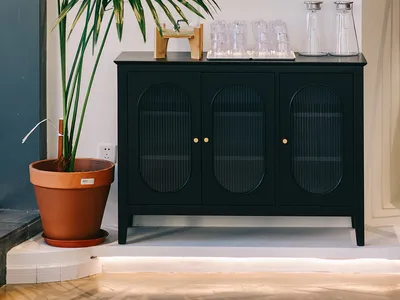 Elegant living space with a glass-fronted cabinet serving as a bar or display case, featuring wine glasses and a potted plant, with a sophisticated atmosphere