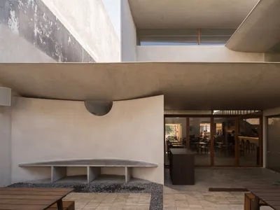 Open modern restaurant with concrete walls, wooden tables, and pendant lighting