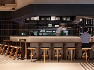 A casual restaurant interior with a bar and three chairs, one person sitting at the bar, creating a welcoming atmosphere