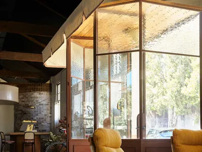 A modern living room with a yellow chair, dining table, couches, and a potted plant, well-lit by natural sunlight