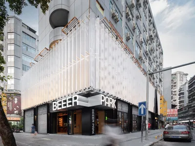 一間熱鬧的白色立面餐廳，設有戶外座位區，以及醒目的「Beer Park」招牌，背景為模糊的人群與周遭環境