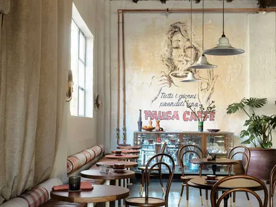 A restaurant dining area with tables, chairs, artwork on the walls, and a bar offering additional seating and a cozy atmosphere