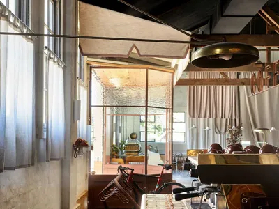 A modern kitchen with a dining table, chairs, and various items on the surfaces, surrounded by wood flooring and glass windows, with a well-lit and welcoming atmosphere
