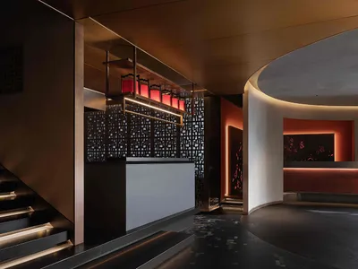 Modern hotel lobby with a circular counter area featuring a bar, sinks, and a mix of wood and tile flooring, set against a warm white and brown color scheme