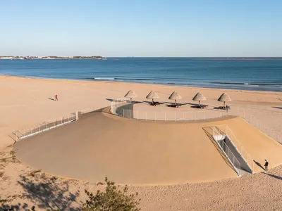 A modern beachside restaurant with a large dome structure housing several umbrellas, surrounded by a beautiful ocean view