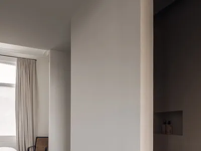 一間光線柔和的臥室，配有白色床鋪與兩把椅子，周圍環繞白色牆面，呈現極簡風格