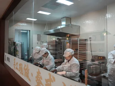專業廚房場景，四名戴白帽工人隔著玻璃屏風準備食物，周圍環繞廚房家電