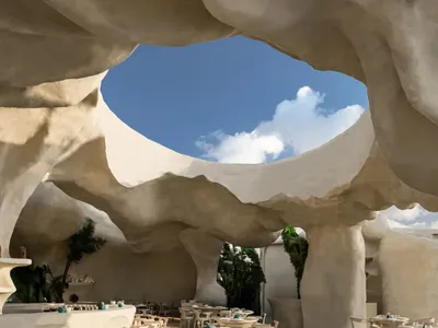 寬敞的餐廳內部，白色石材牆面、多張桌椅與盆栽植物，營造出乾淨清爽且溫馨的氛圍