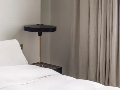 A cozy bedroom with a white bed, a black and gold lamp on each side, and a chair near the foot of the bed