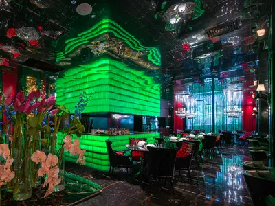綠牆與酒吧區的現代餐廳內部，包含餐桌、椅子、花瓶與瓶子