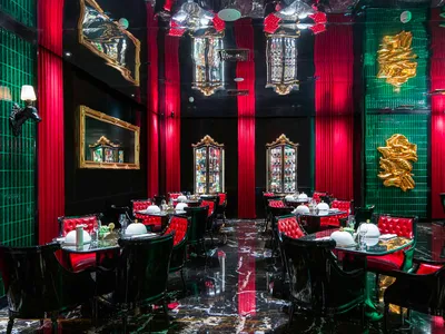 Modern restaurant interior with red walls, black accents, and tables and chairs, featuring wine glasses and a bar