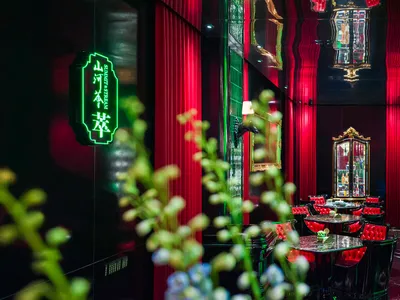 Warm and inviting Asian restaurant interior with red walls, green neon lights, chairs, tables, and a bar area with a countertop and decorative items