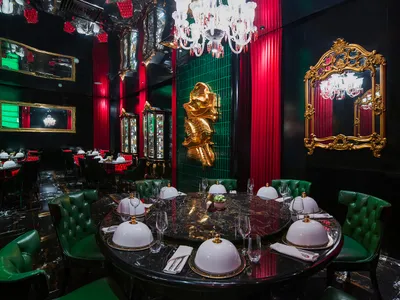 Elegant dining area with a table set for a meal, surrounded by chairs, in a room with red walls and a chandelier