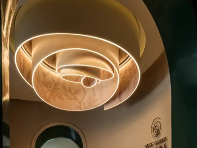 A hotel lobby with a circular ceiling light fixture, chairs, and a potted plant, creating a warm atmosphere