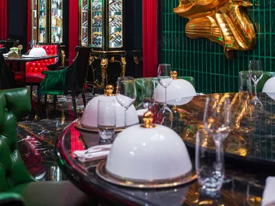 Luxurious dining area with a gold statue centerpiece, red leather chairs, and wine glasses on a table surrounded by books