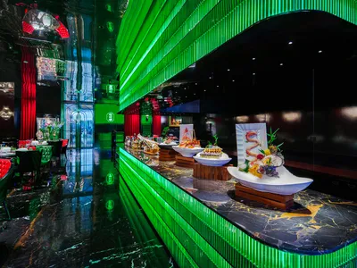 A modern restaurant dining area with multiple tables, green accents, potted plants, and bowls of food on the tables