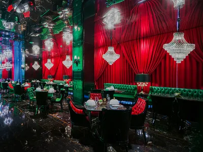 Ornate restaurant interior with red velvet walls, green accents, and cozy dining area with tables and chairs