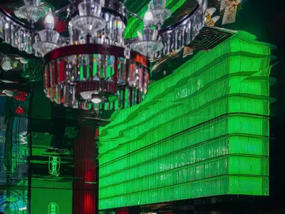 現代餐廳內部，綠色牆面、吧台區，以及鋪白桌布的餐桌與各式碗盤，背景為廚房