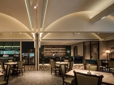 A lively restaurant interior with multiple tables, chairs, and decorative items such as bottles, vases, and potted plants, set in a modern and stylish environment