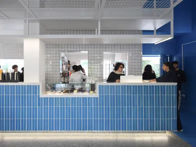 A bustling restaurant counter with people waiting in line to order food and drinks, surrounded by cups and a lively atmosphere