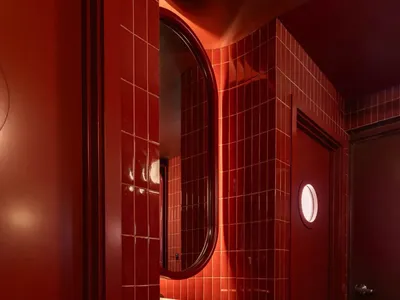 Bathroom with two sinks, one with a mirror, and red walls, set in a well-lit space with natural light